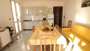 Un comedor con una mesa dispuesta para dos, un sofá amarillo y una cocina al fondo.