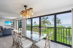 A spacious room with a large glass table, comfortable seating, and a view of the ocean. - Kings Crown 118: Remodeled 3 BR Gulf Front Condo! (Sanibel)