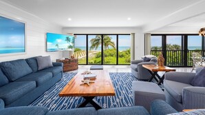A modern living room with a large window offering a view of the beach and palm trees. - Kings Crown 118: Remodeled 3 BR Gulf Front Condo! (Sanibel)