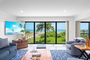 A modern living room with a large sliding glass door leading to a balcony with a view of the beach.