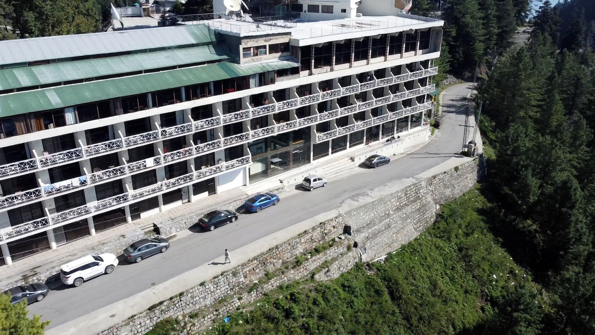 Un hotel de varios pisos con balcones, un estacionamiento y un muro de contención de piedra.