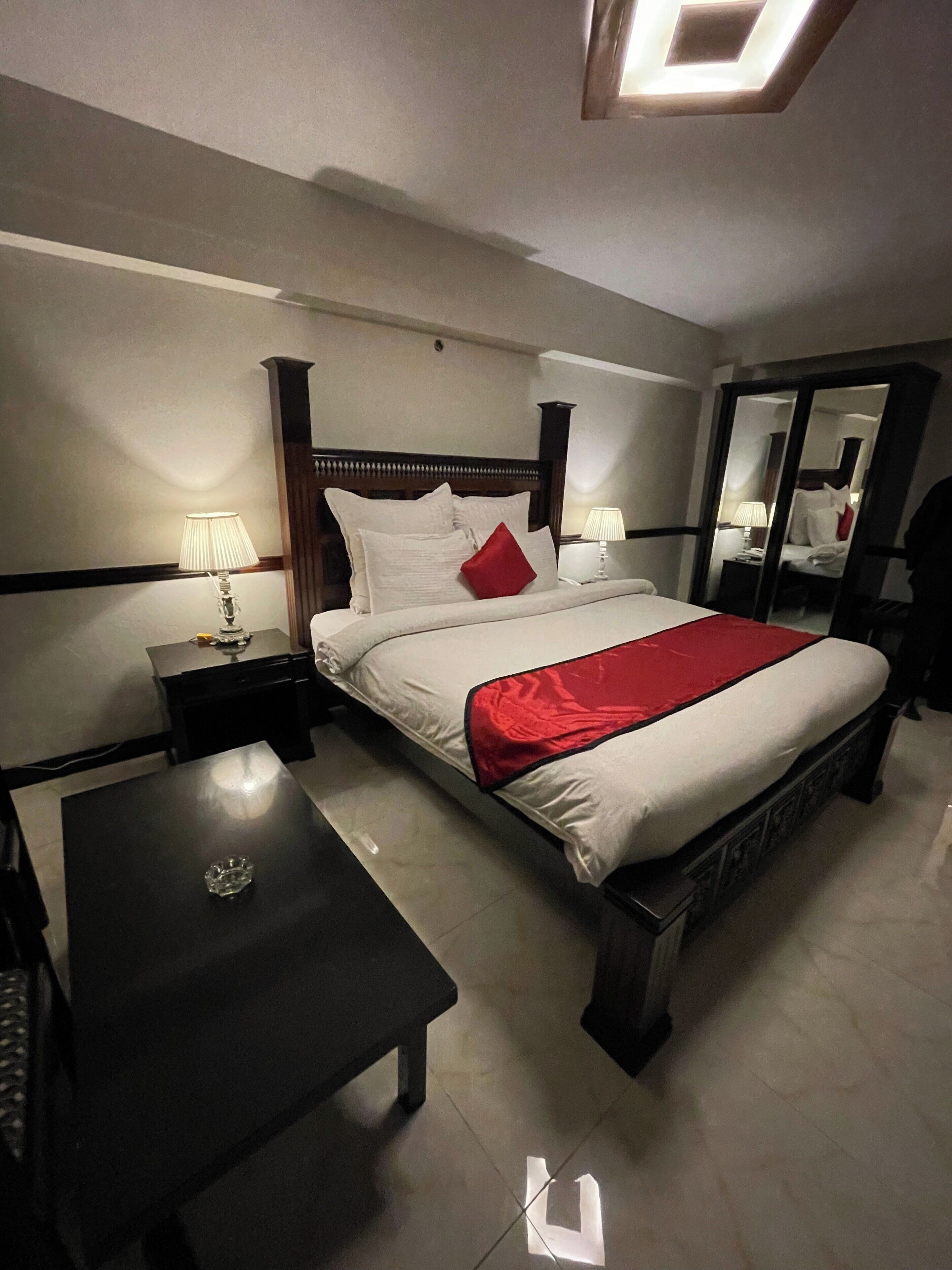 Ein Hotelzimmer mit Bett, Nachttischen, einem Schreibtisch und einem Spiegel.