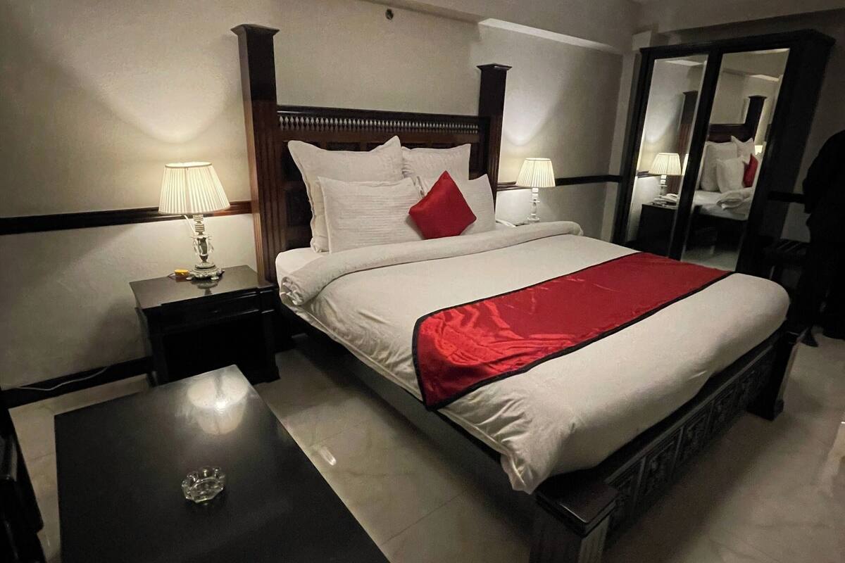 A hotel room with a bed, bedside tables, a desk, and a mirror.