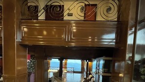 Un vestíbulo amplio con una imponente escalera que conduce a un segundo piso, con barandales decorados y vistas a la ciudad.
