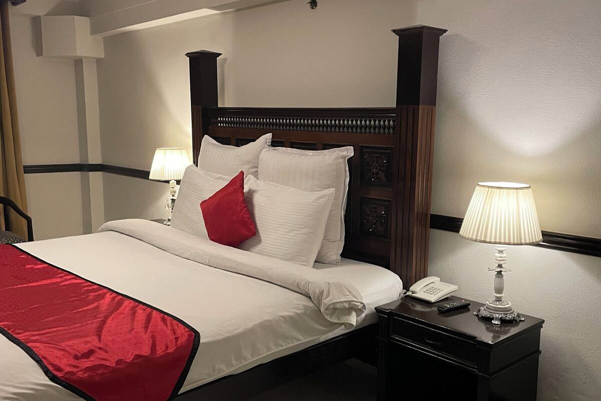 A hotel room with a neatly made bed, a bedside table with a lamp, and a telephone.
