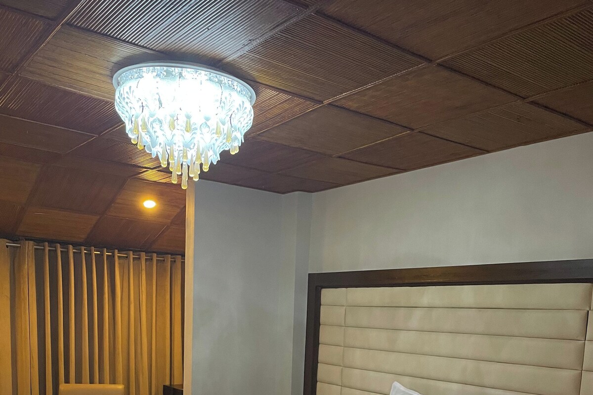 Habitación de hotel con una cama grande, una silla, una mesita de noche, un candelabro y una alfombra estampada.
