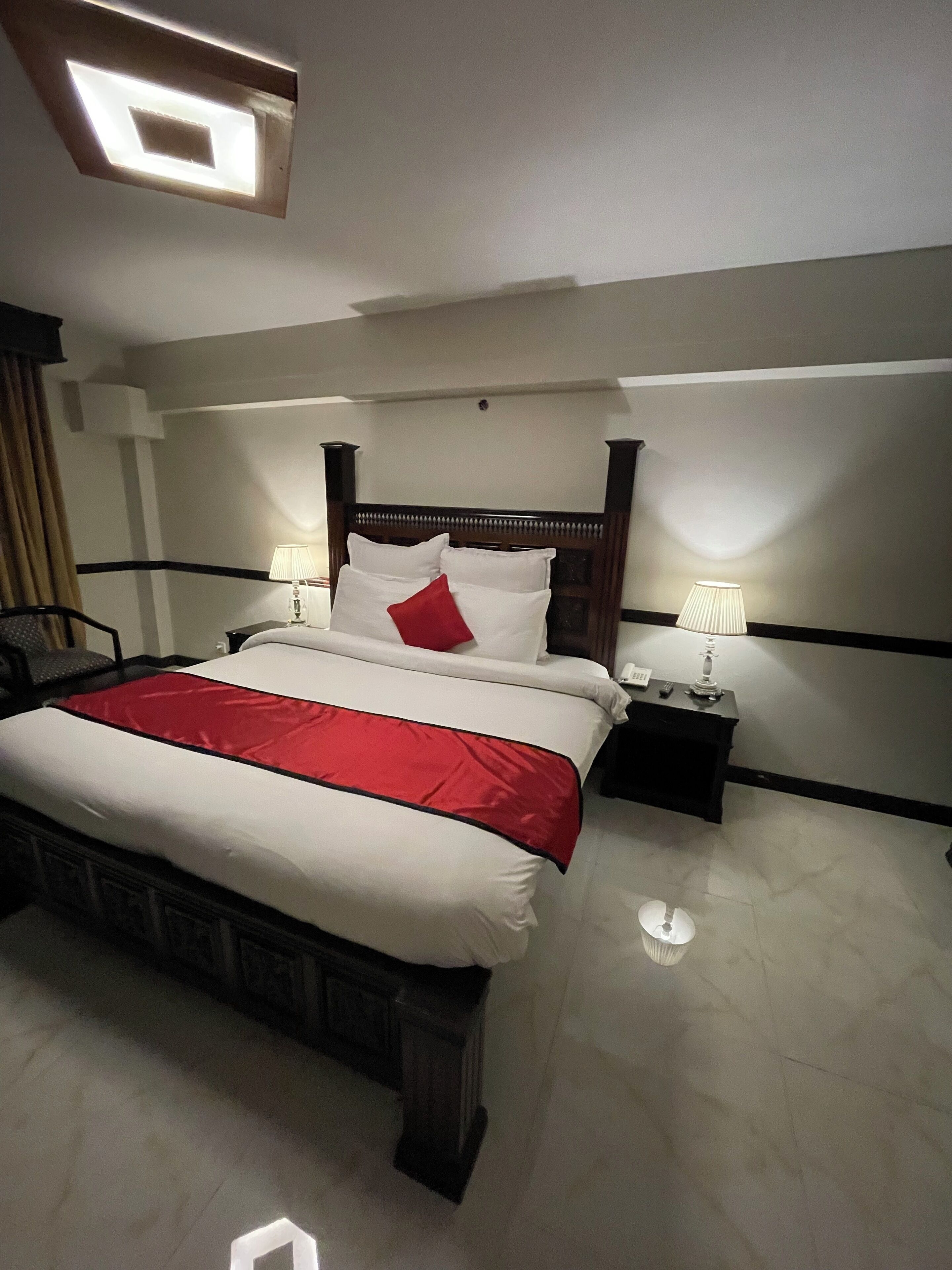 Habitación de hotel con una cama grande, dos mesitas de noche, un cabecero y una lámpara en el techo.