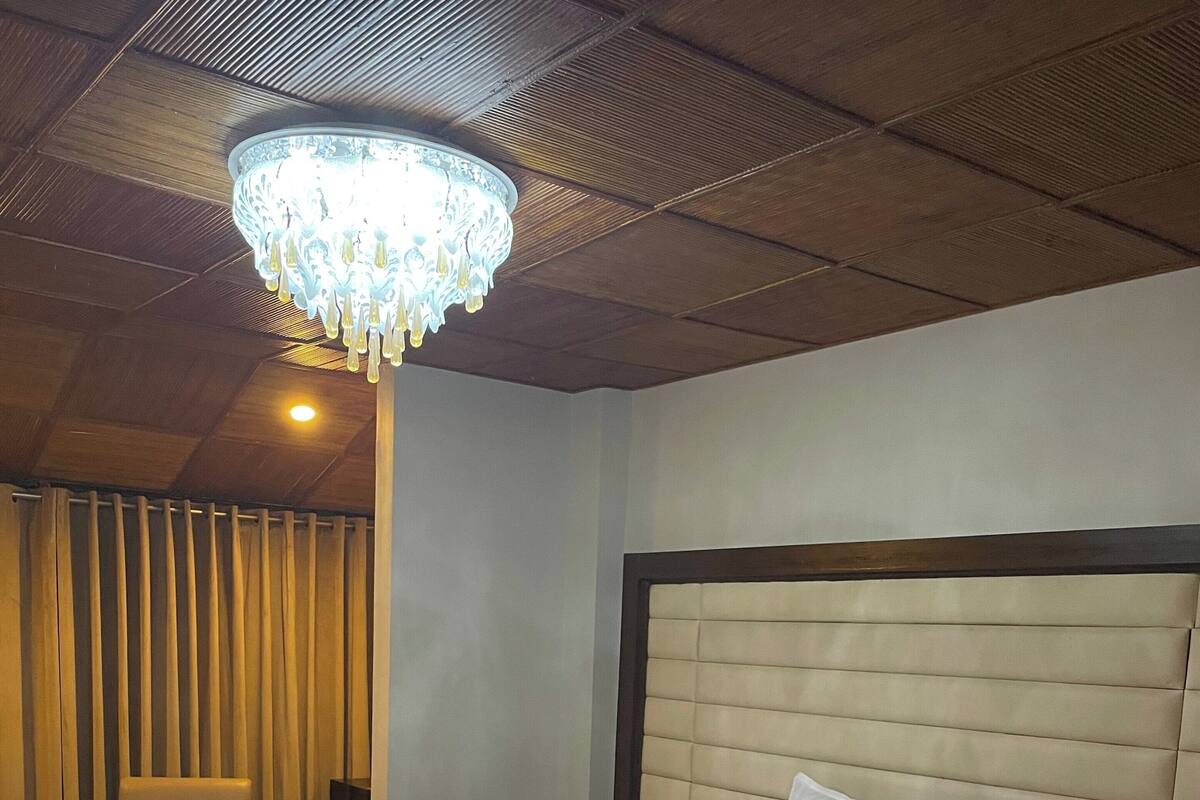 A hotel room with a large bed, a chair, a nightstand, a chandelier, and a patterned rug.
