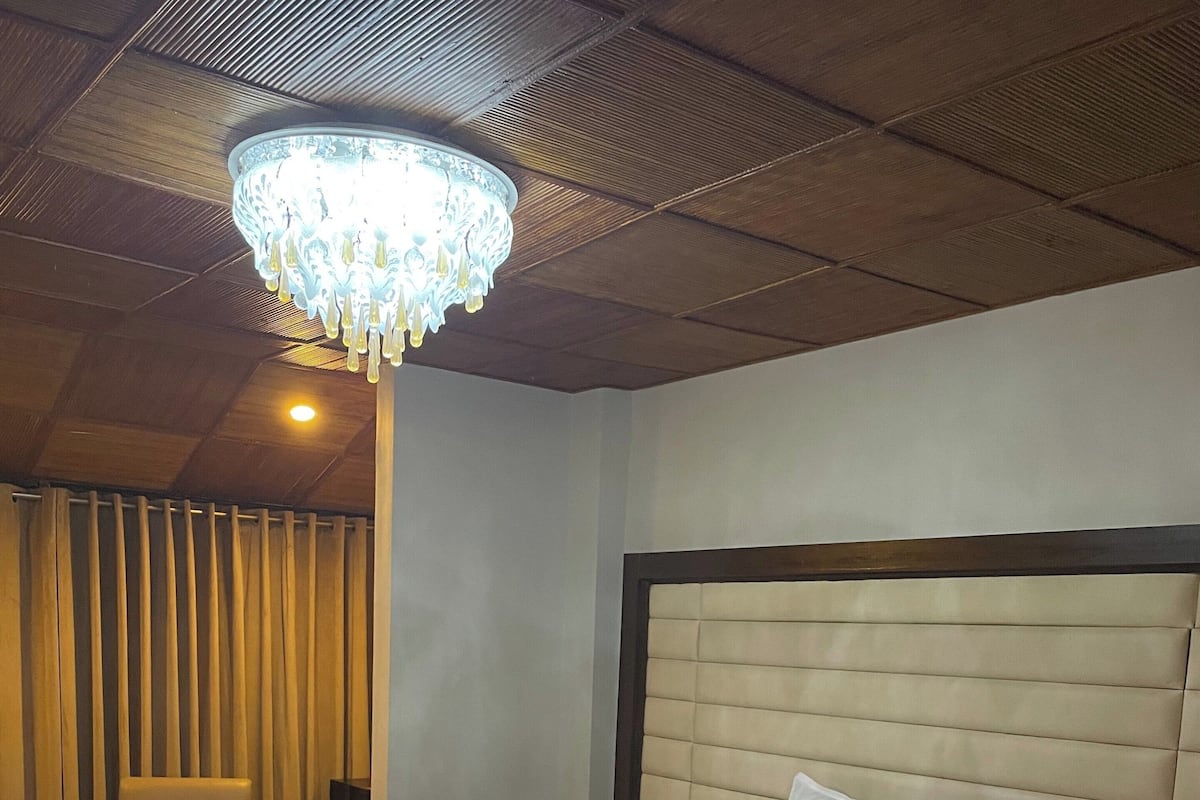 Ein Hotelzimmer mit einem großen Bett, einem Sessel, einem Nachttisch, einer Kristallleuchtre und einem gemusterten Teppich.