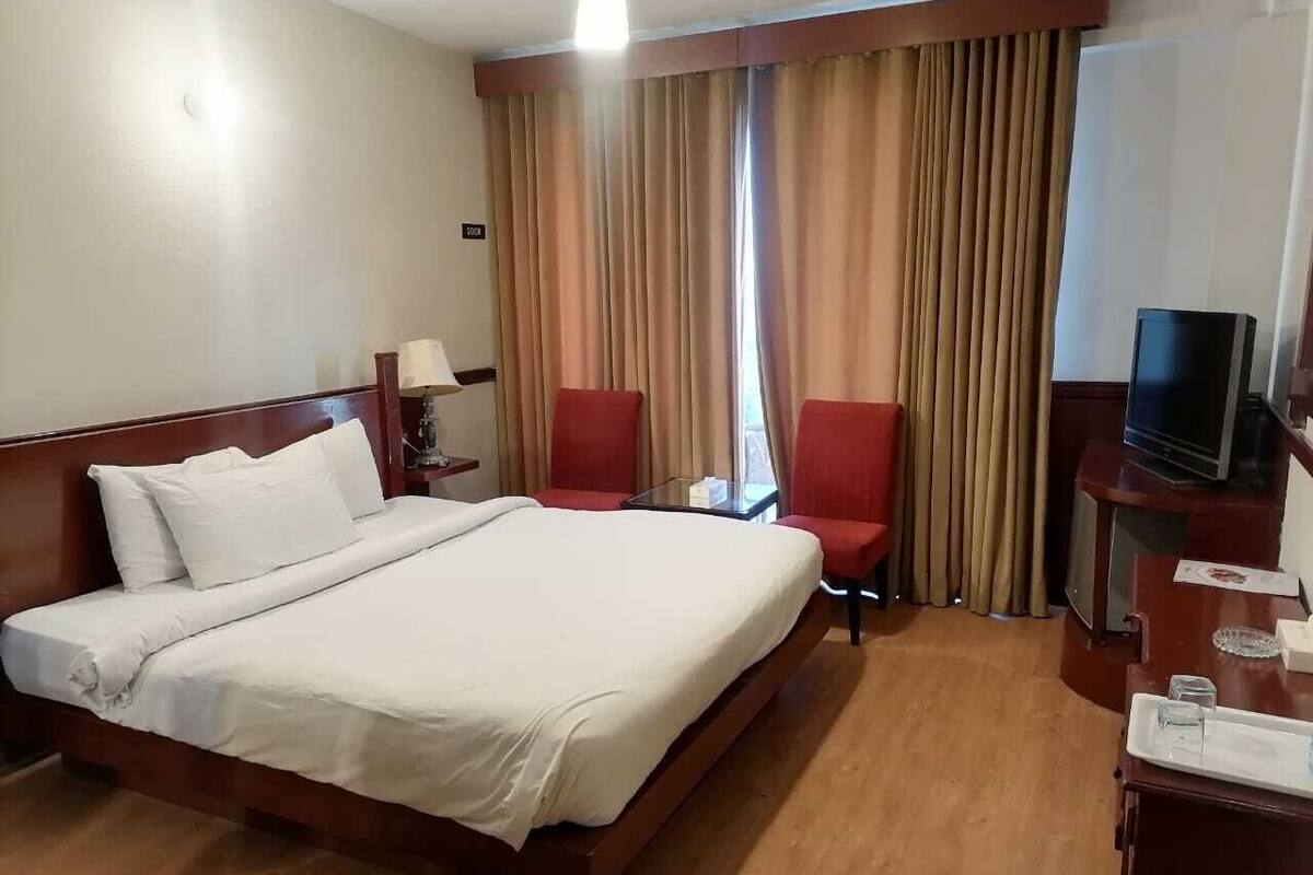 A hotel room with a large bed, two red chairs, a TV, and a desk with a lamp.