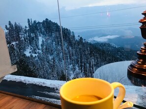 Una taza amarilla sobre un alféizar con vistas a una montaña nevada.