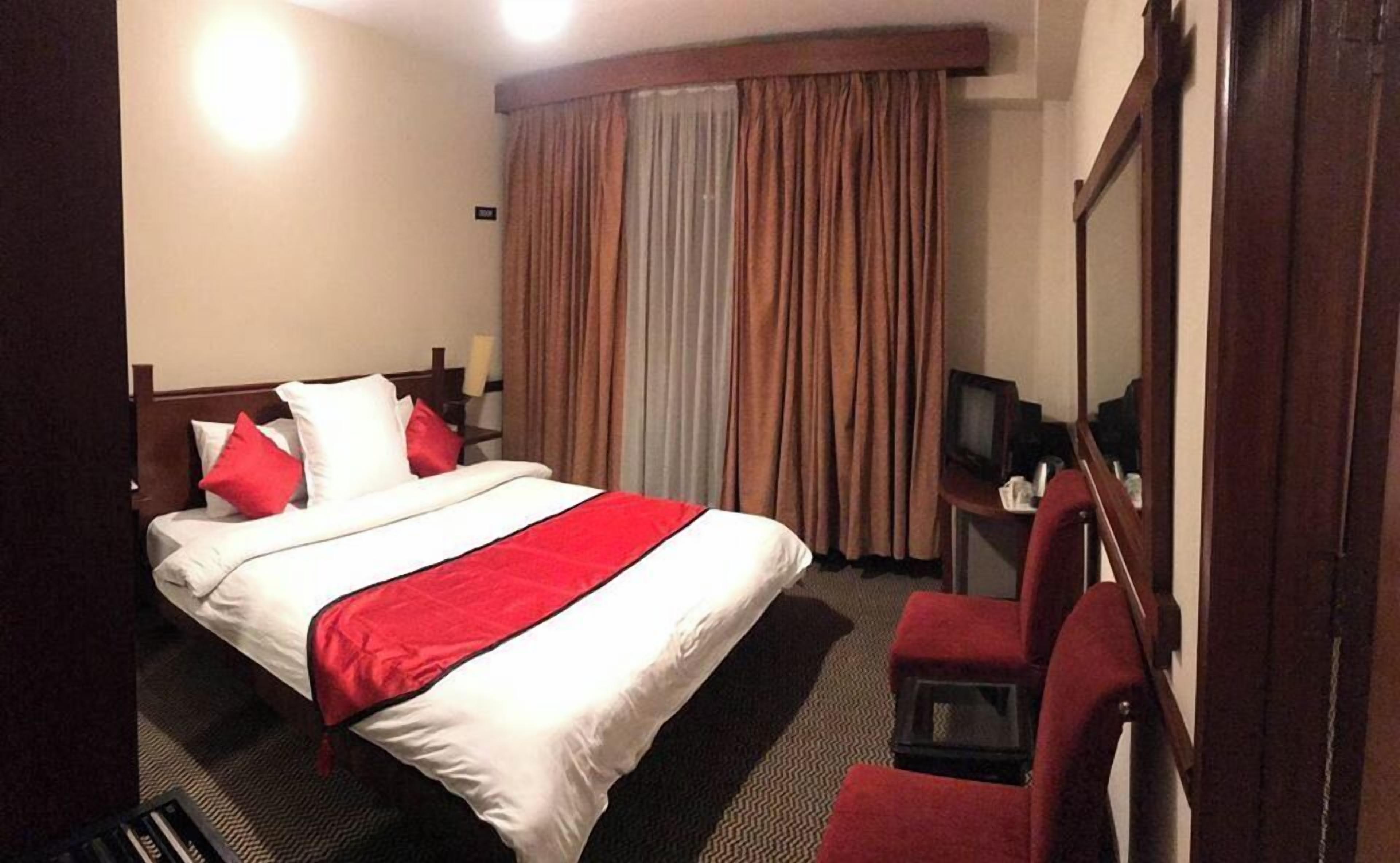 A hotel room with a bed, a desk, a chair, a television, and curtains.