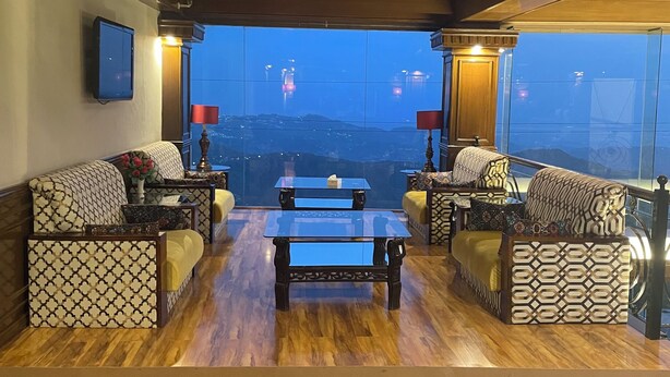 Una sala de estar moderna con piso de madera, sofás estampados, una mesa de centro de vidrio y vista a la ciudad al anochecer.