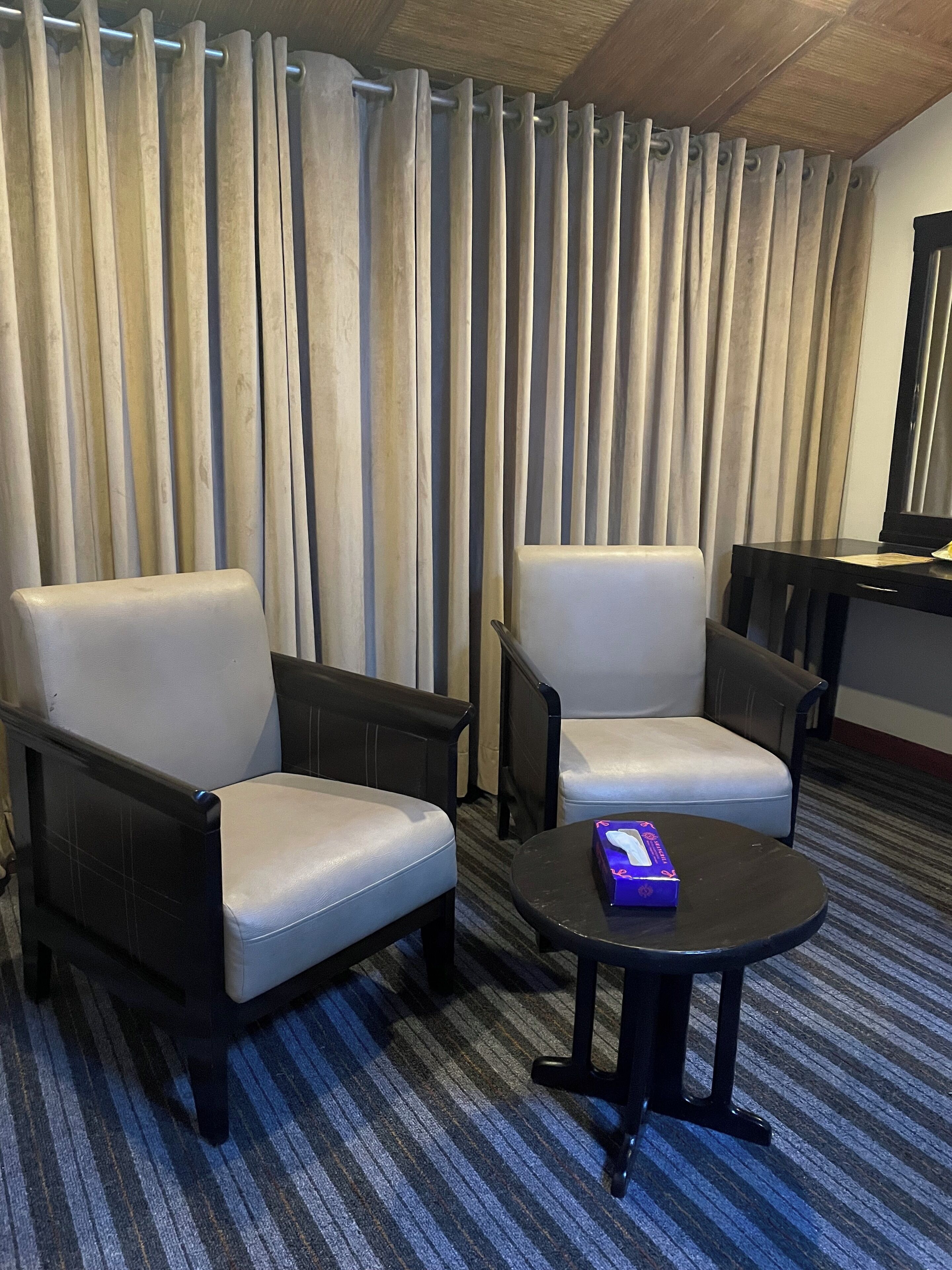 Ein Hotelzimmer mit zwei Ledersesseln, einem kleinen runden Tisch und einem Schreibtisch mit Stuhl.