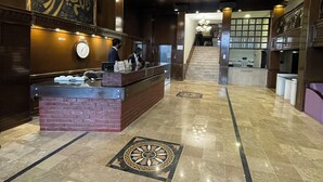 Un hall con mostrador de recepción, un reloj y una escalera que lleva a otra zona.