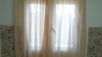 A room with two bedside tables, a window with curtains, and floral wallpaper.