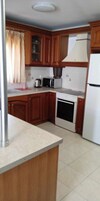 Una cocina con armarios de madera, un lavamanos de acero inoxidable, una encimera blanca, una estufa y un refrigerador.