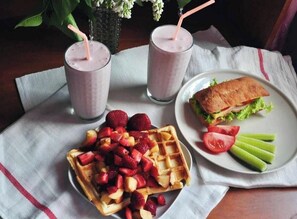 A breakfast setting with waffles topped with strawberries, a sandwich with lettuce and tomato, and two smoothies with straws. - IONIAN Residence houses (Kefalonia)