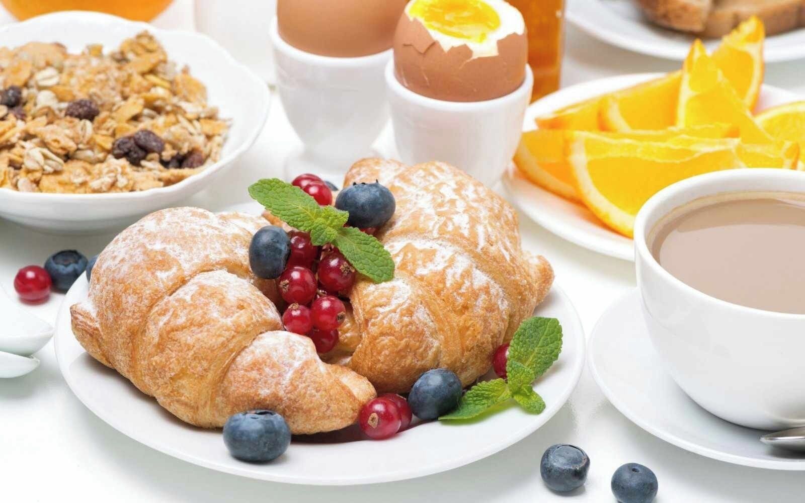 A breakfast setting with a croissant, blueberries, red currants, orange slices, and a cup of coffee.