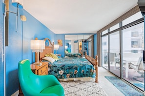 A bedroom with a large bed, a green chair, and a view of the outside through a sliding glass door. - Includes Xplorie Activities and Linens. PYRAMID - 1BR Veranda condo w/outdoor pool. (Ocean City)