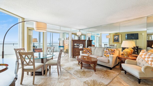 A spacious living room with a glass dining table, comfortable seating, and a large window offering a view of the ocean. - Includes Xplorie Activities and Linens. PYRAMID - 1BR Veranda condo w/outdoor pool. (Ocean City)
