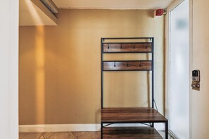 Una esquina de una habitación con una pared texturizada color beige, un perchero metálico y un banco de madera.