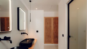 A modern bathroom with a black sink, a mirror with a light, and a wooden door in the background. - Ios Bliss (Ios)