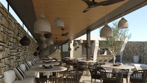 An outdoor dining area with round tables and chairs, stone walls, and hanging pendant lights. - Ios Bliss (Ios)