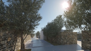 A pathway flanked by stone walls and trees, leading to a building with a clear sky above. - Ios Bliss (Ios)