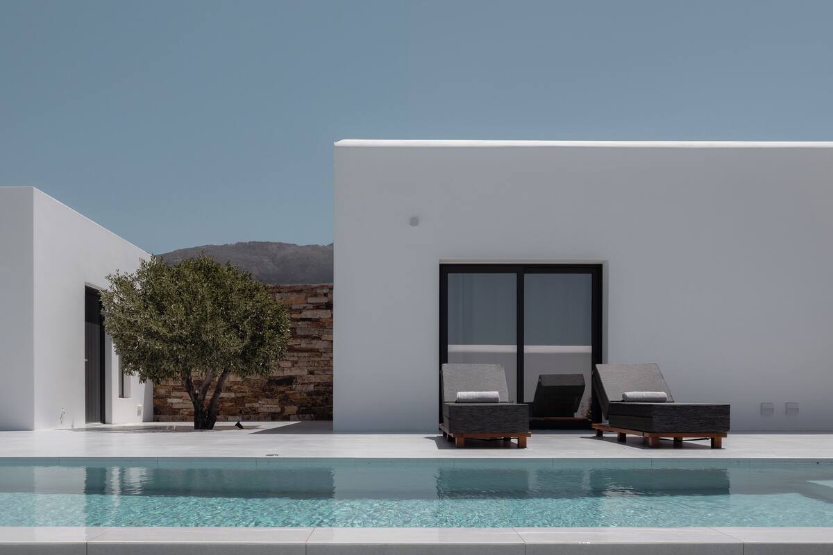 A modern poolside area with two lounge chairs, a clear pool, and a stone wall.