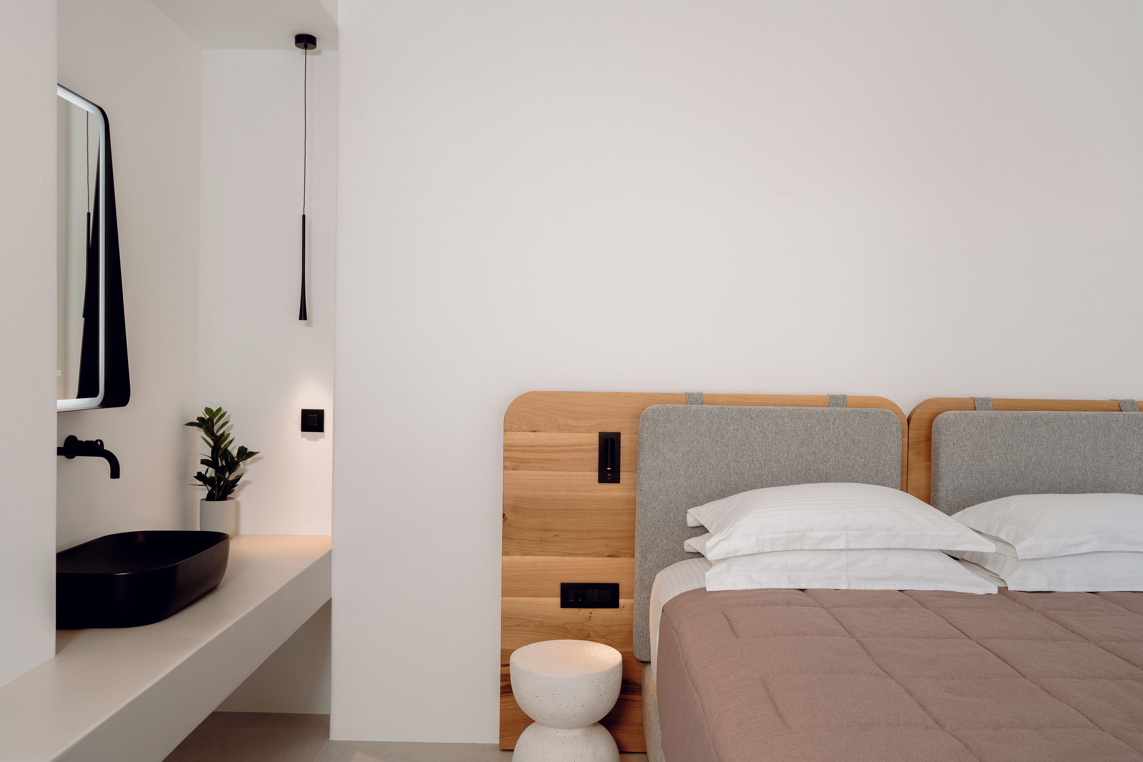 A modern bedroom with a wooden headboard, a bedside table, a black sink, and a small plant.