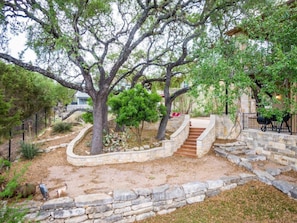 A stone staircase leading up to a building, surrounded by trees and a stone wall.