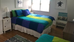 A bedroom with a bed, bedside tables, a window with curtains, a wall-mounted picture, and a small shelf with decorative items.