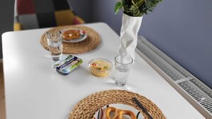 A dining table with two plates, each with a pretzel and a knife, and a small glass of water. There are also two packaged snacks and a vase with flowers. - Haus Valentonio Einz (Zeltingen-Rachtig)