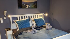 A bedroom with a white bed, blue bedding, and a painting of a landscape on the wall. - Haus Valentonio Einz (Zeltingen-Rachtig)