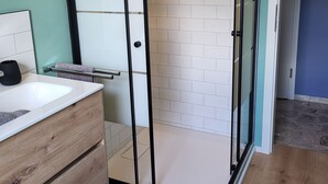 A modern bathroom with a glass-enclosed shower, white tiled walls, a wooden vanity, and a small shelf. - Haus Valentonio Einz (Zeltingen-Rachtig)
