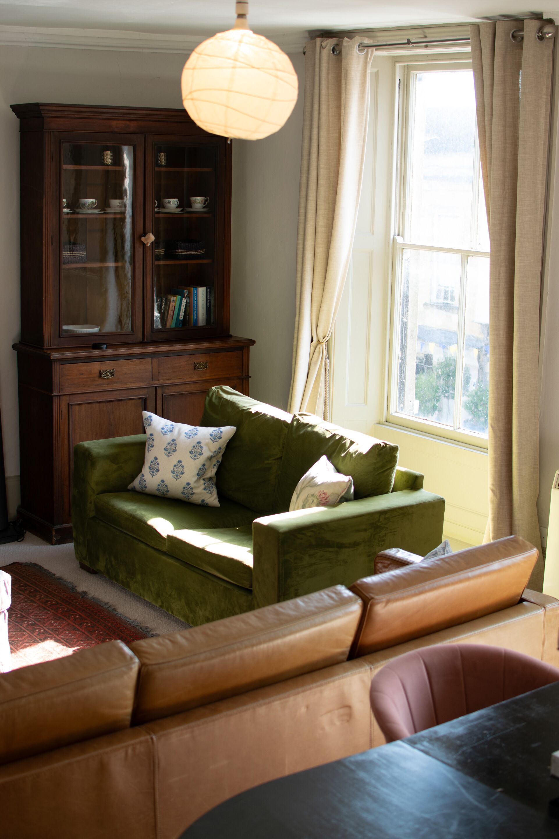 Una sala de estar con un sofá verde, un mueble de madera y una ventana con cortinas.