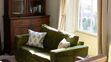 Una sala de estar con un sofá verde, un mueble de madera y una ventana con cortinas.