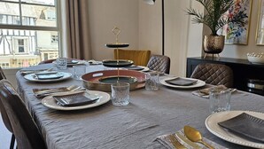 Une table à manger dressée avec des assiettes, des couverts et des verres, agrémentée d’un centre de table décoratif et d’une plante en pot placée sur le côté.