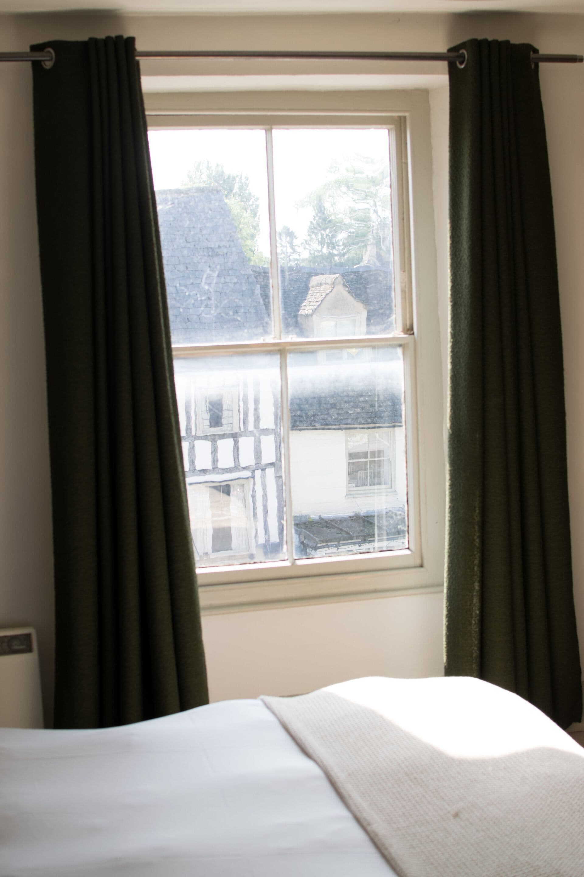 Una habitación con cama, ventana con cortinas y vista a una casa.