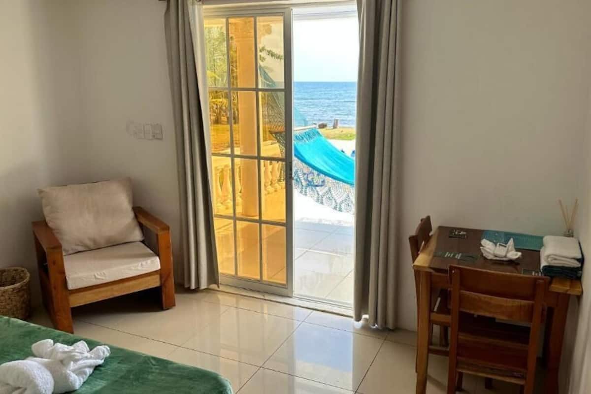 Una habitación con cama, una silla, una mesa y vista al mar a través de un ventanal corredero.