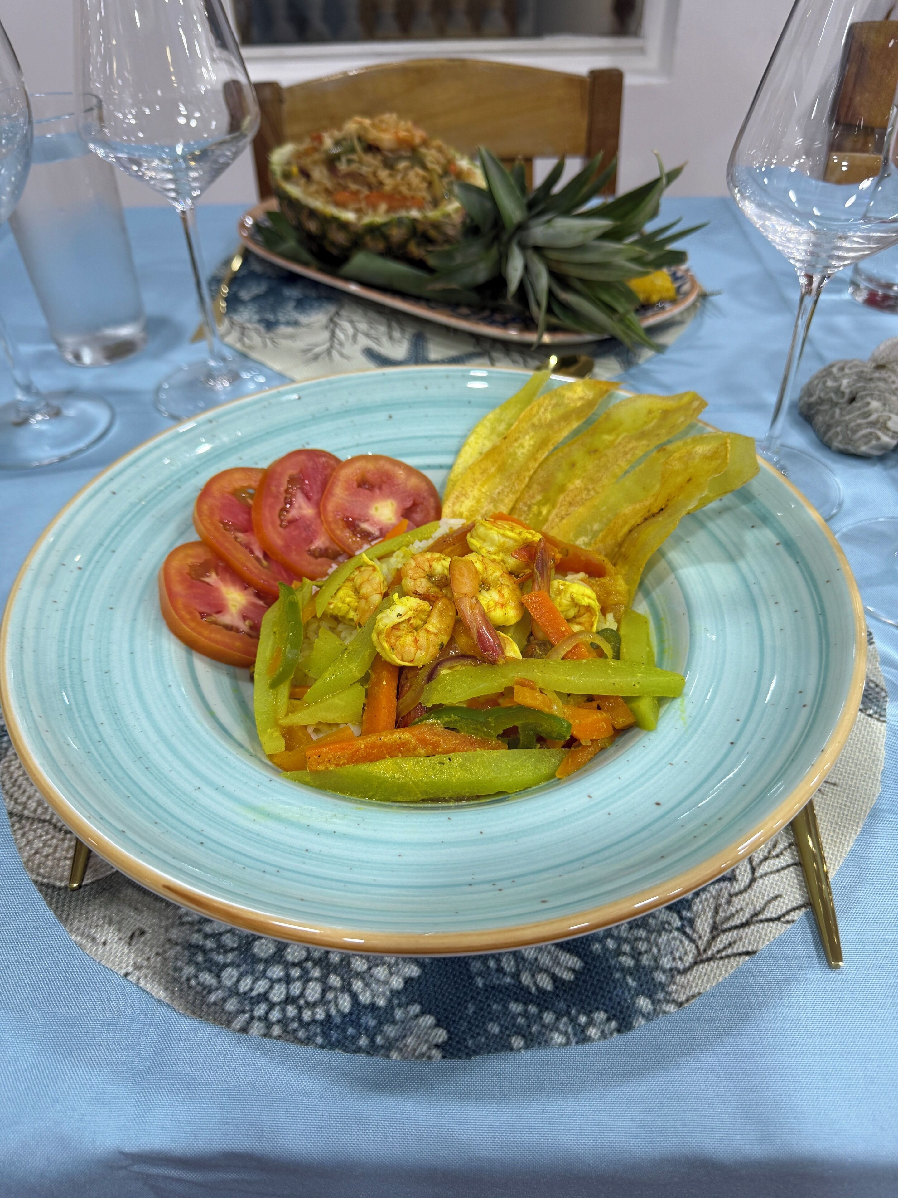 Ein Teller mit Garnelen, Gemüse und Ananas auf einer blauen Tischdecke.
