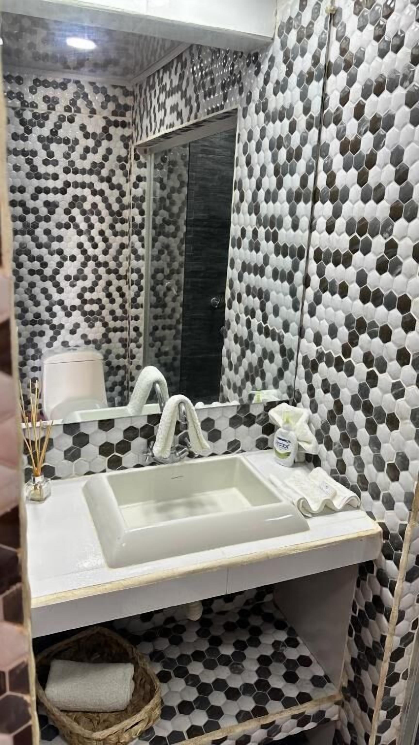 Een badkamer met een witte wastafel, een spiegel en een zwart-wit patroon op de muur.