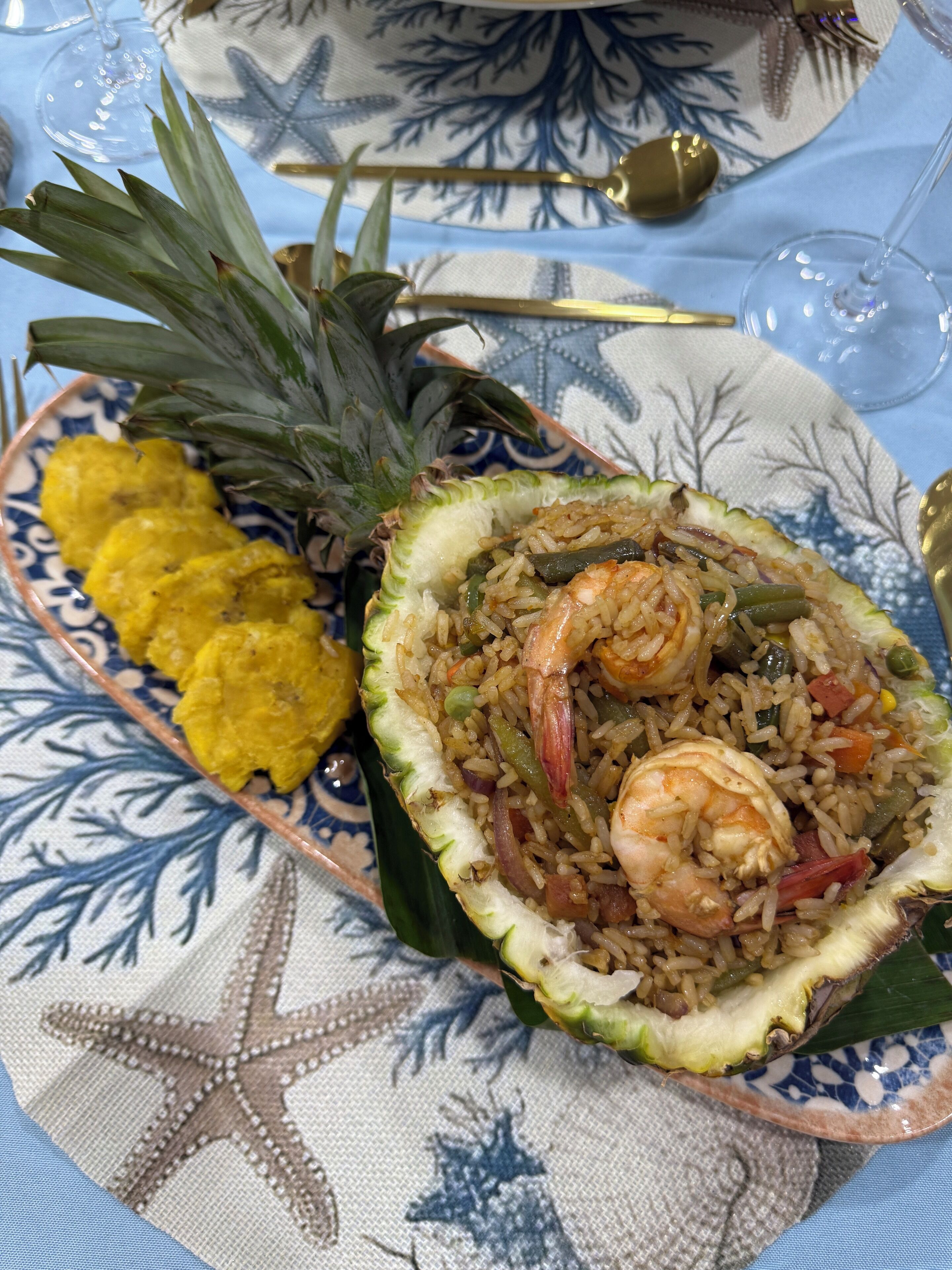 A plate of fried rice with shrimp, vegetables, and a pineapple on a decorative plate.