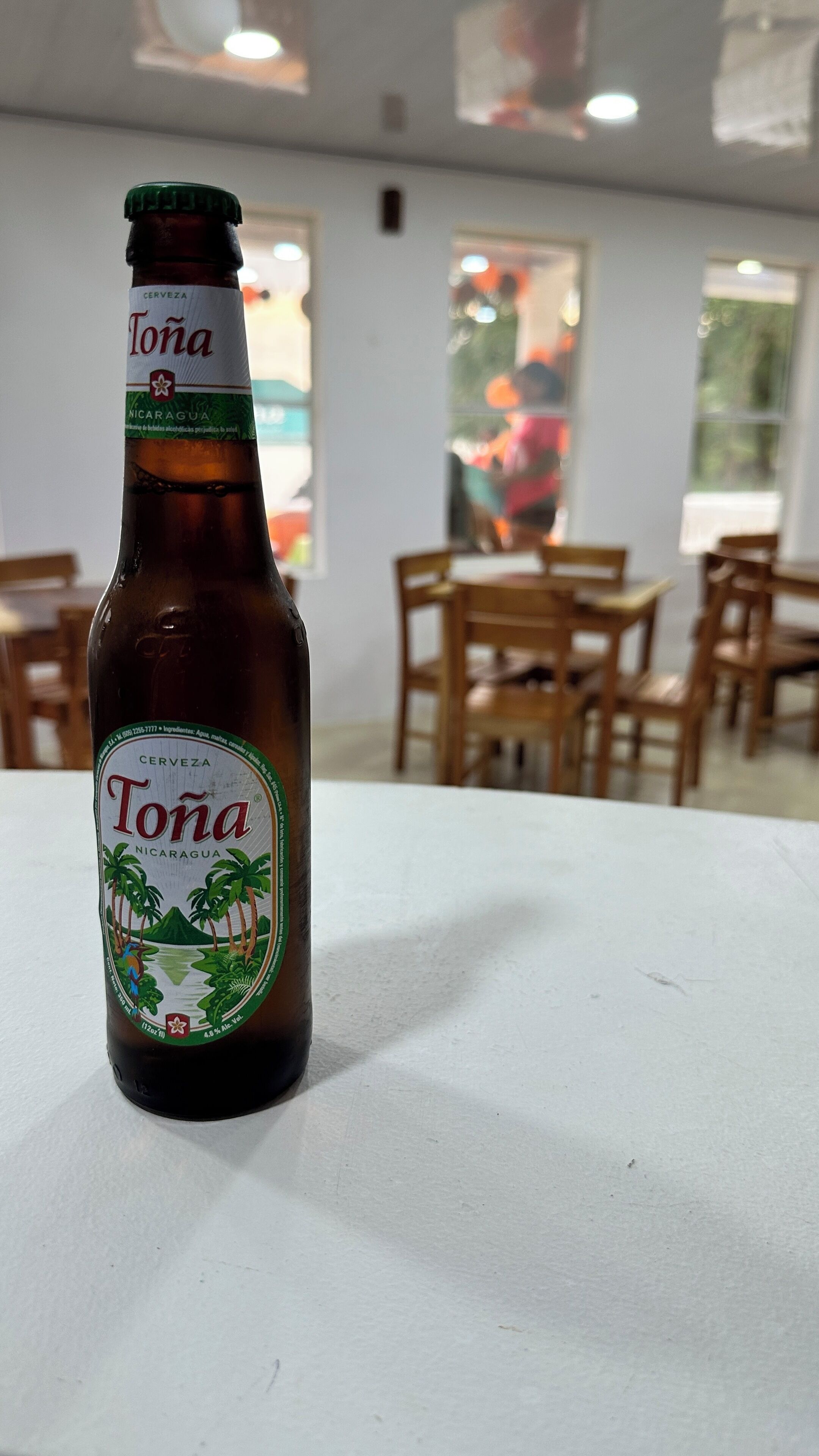 Een fles Tona bier op een tafel in een kamer met houten stoelen en tafels.