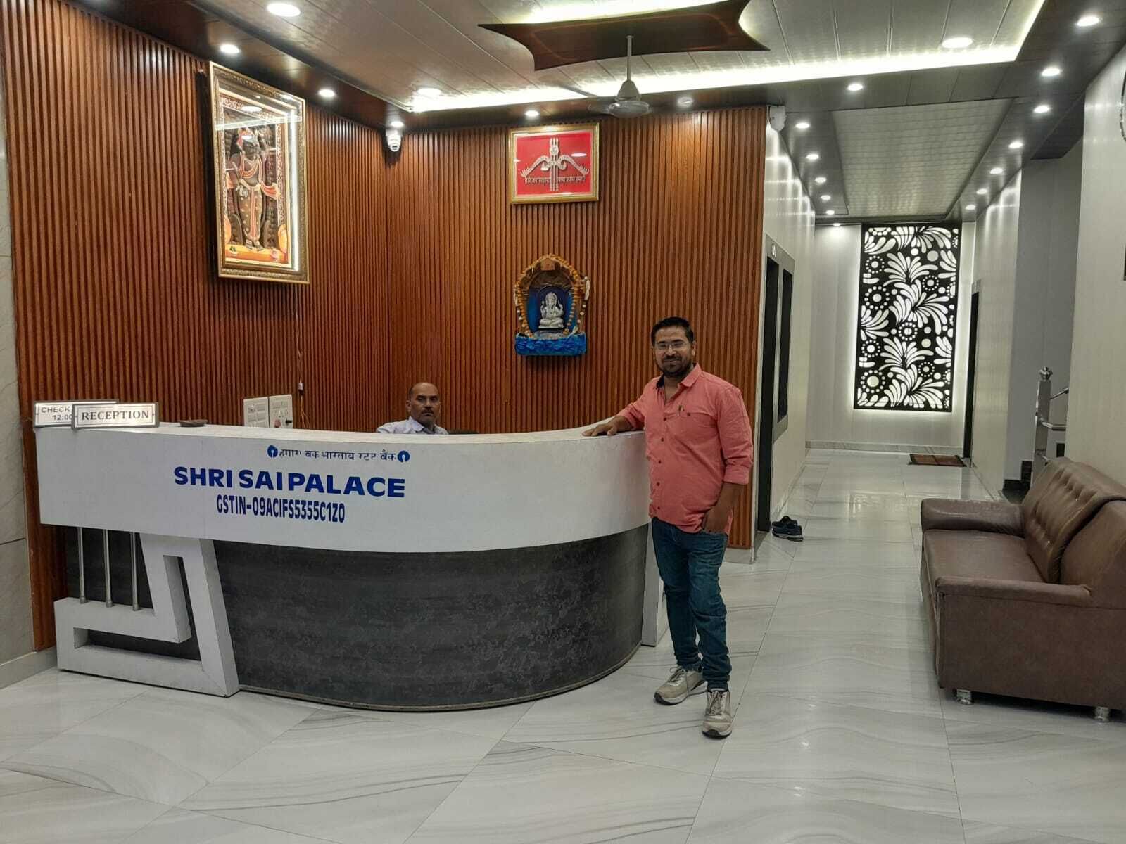 A reception desk with a sign reading "SHRI SAIPALACE" and a man standing beside it.