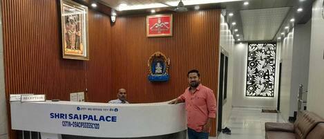 A reception desk with a sign reading "SHRI SAIPALACE" and a man standing beside it.