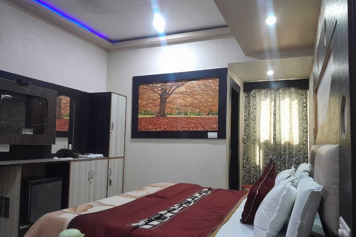 Habitación de hotel con cama, televisor, escritorio y ventana con vista a un árbol.