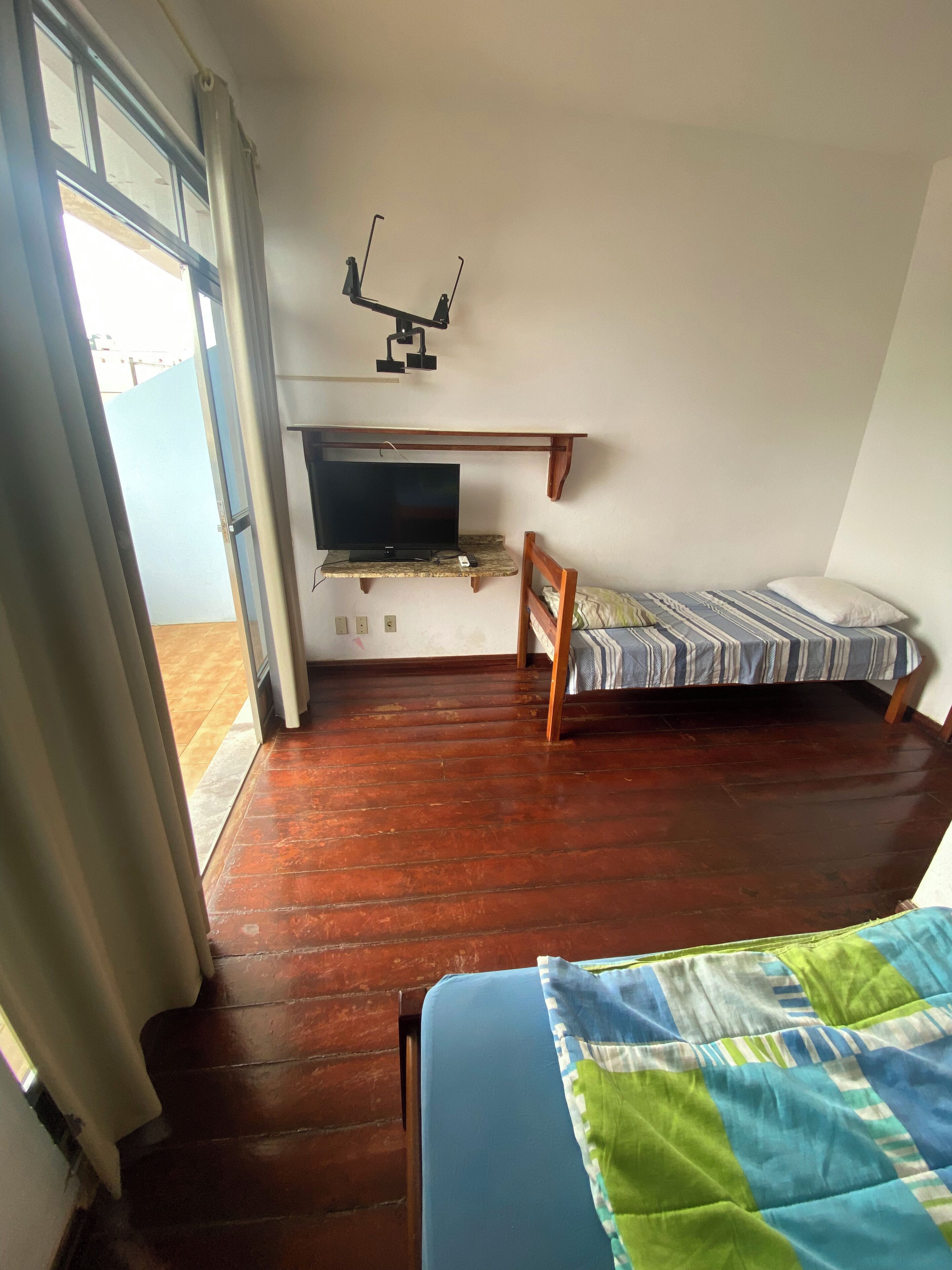 Een kamer met een bed, een televisie op een standaard, een houten stoel en een raam met gordijnen.