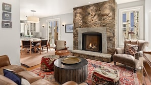 A cozy living room with a stone fireplace, a dining area with wooden furniture, and a kitchen in the background. - Family-Friendly East Aspen Retreat with Hot Tub, Views & Minutes to Downtown (Aspen)